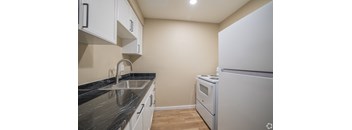 A kitchen with a white refrigerator, sink, and cabinets.