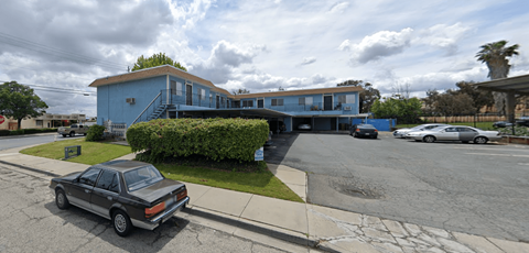 A car is parked on the side of a street in front of a blue building.