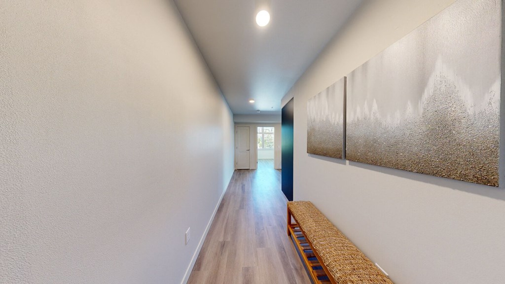 a long hallway with white walls and wood flooring and a painting on the wall