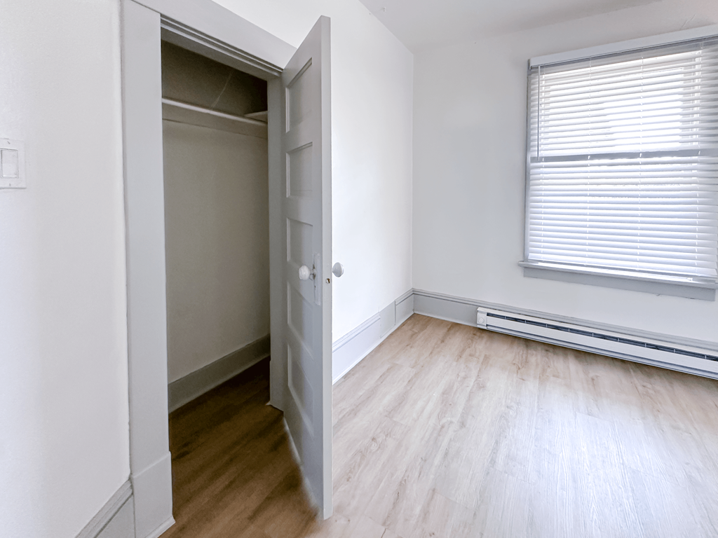 A room with a wooden floor and a window with blinds.