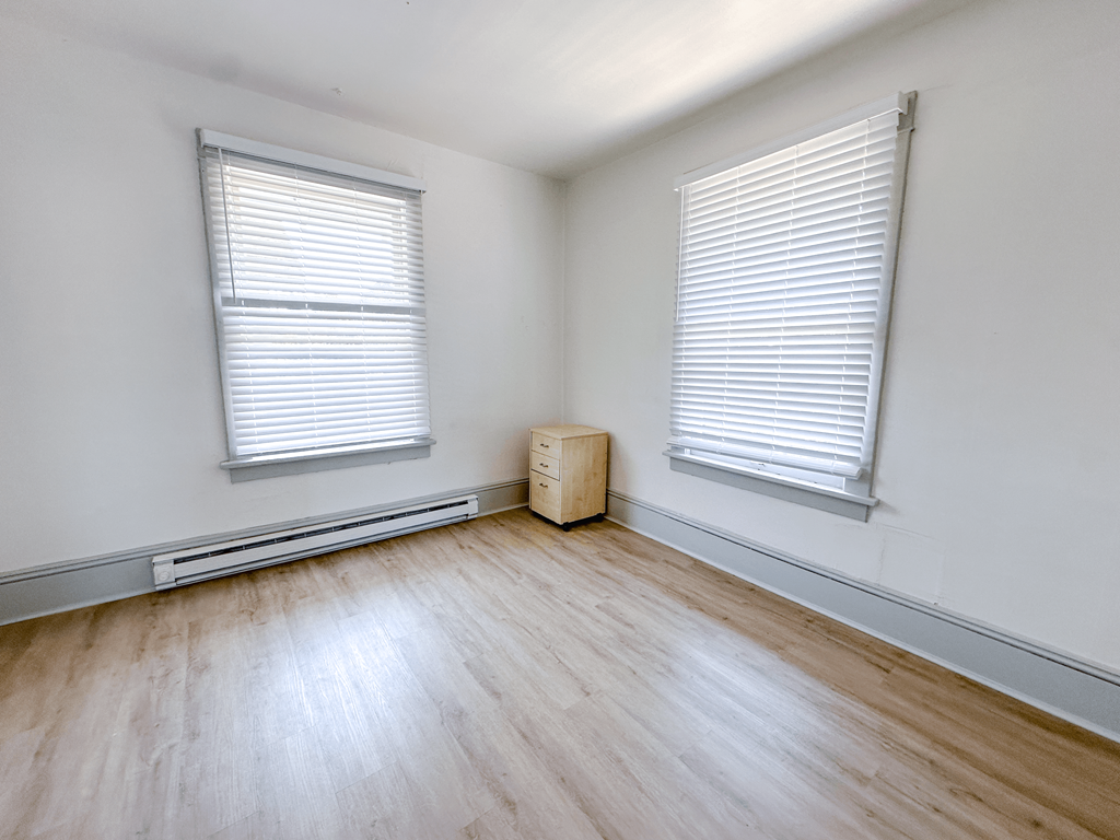 A room with wooden floors and two windows with blinds.