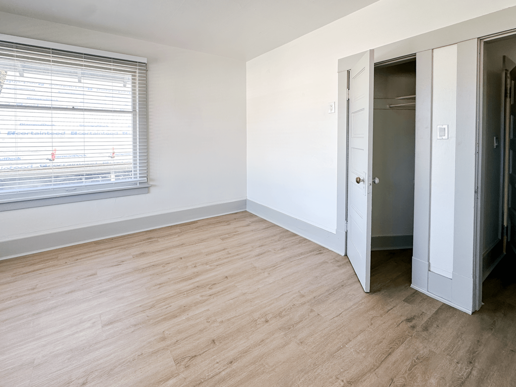 A room with a wooden floor and a window with blinds.