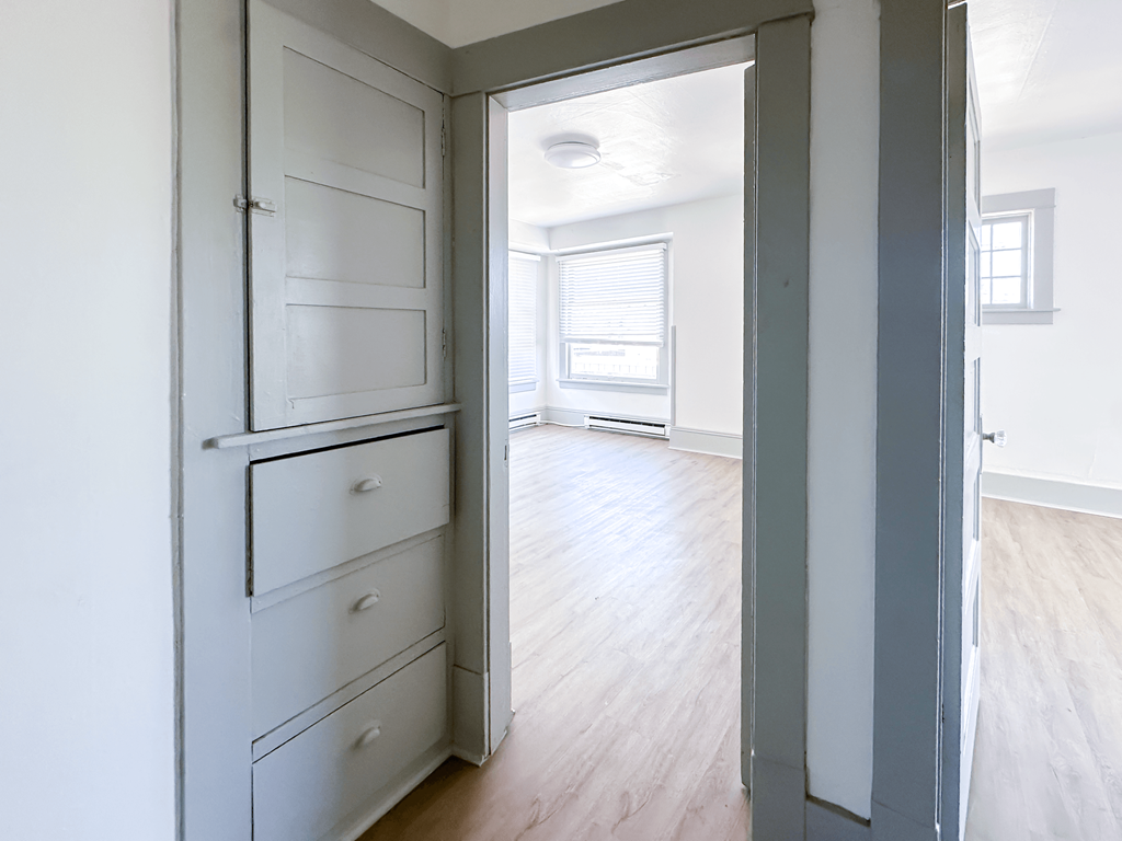A white wardrobe with a mirror above it is open to a room with a window.