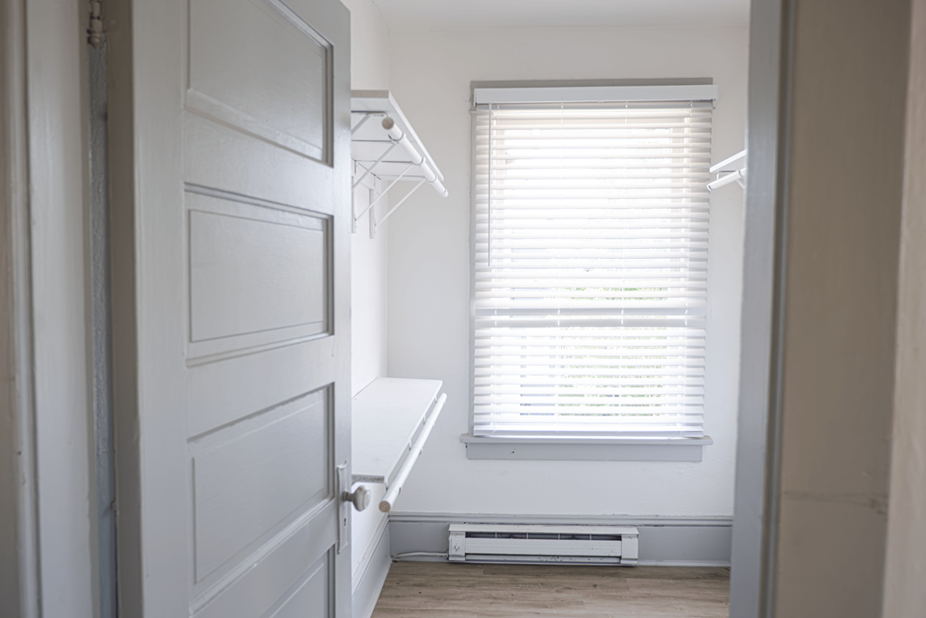 A white door is open to a hallway with a window and a white air conditioner.