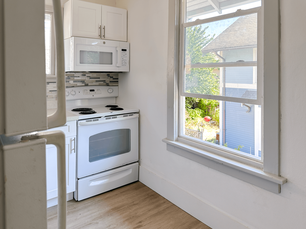 A white kitchen with a window overlooking a house.