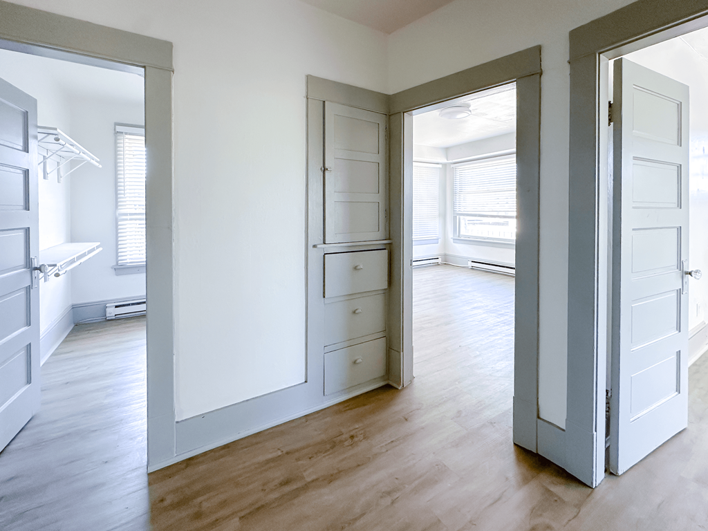 A room with white walls and wooden floors with a white door on the right.