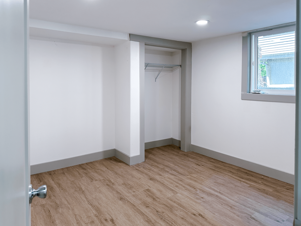 A room with a wooden floor and a white wall with a door and a window.