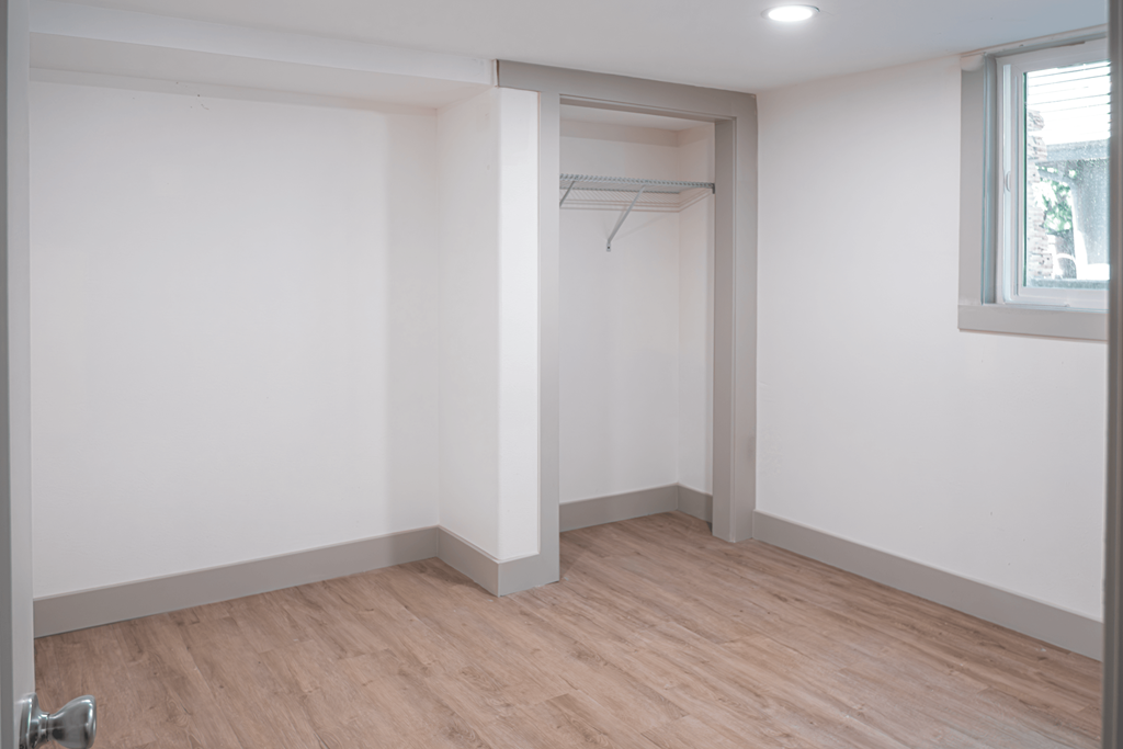 A room with a wooden floor and a white wall with a small window.