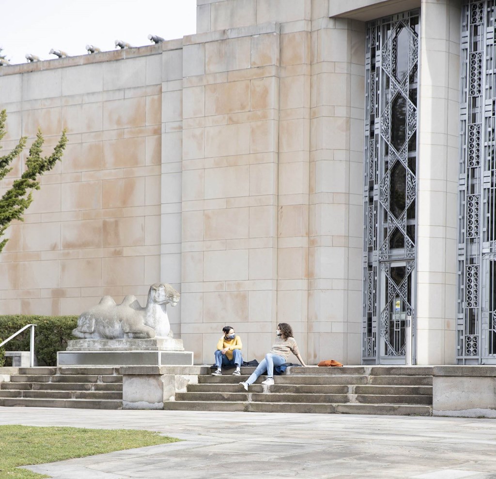 two people sitting on the steps of a building with a lion statue
