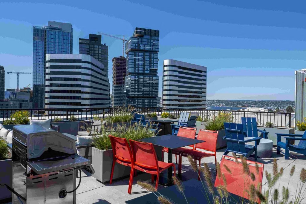 a rooftop patio with tables and chairs and a grill and a city in the background