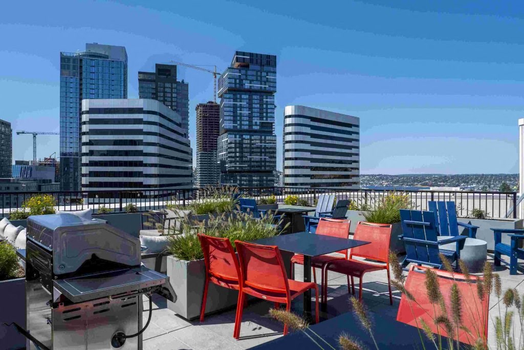 a rooftop patio with tables and chairs and a grill and a city in the background