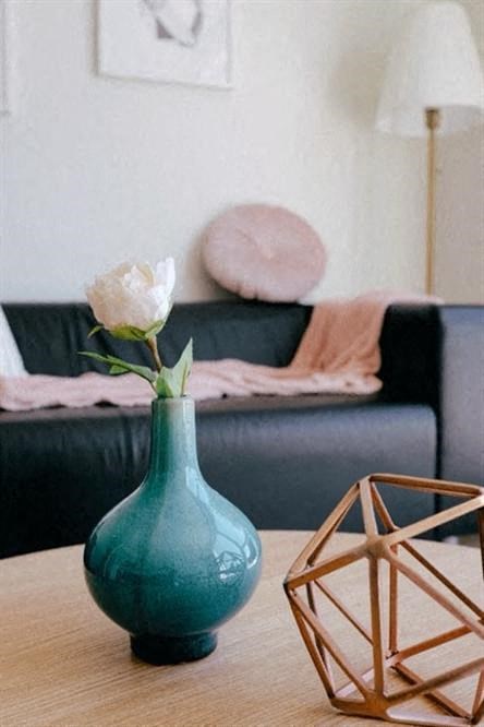 a green vase with a white flower on a table