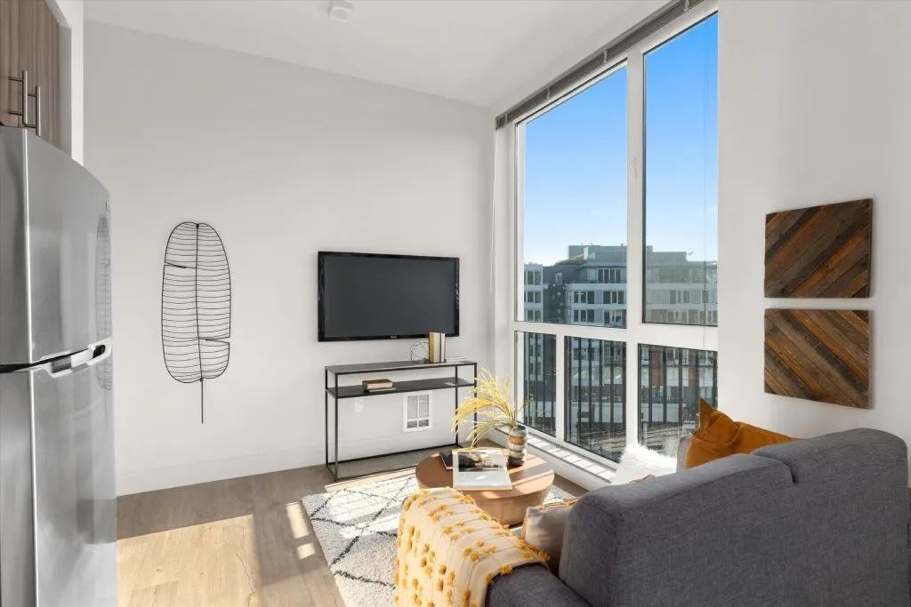 A living room with a grey couch, a television, and a window overlooking a cityscape.