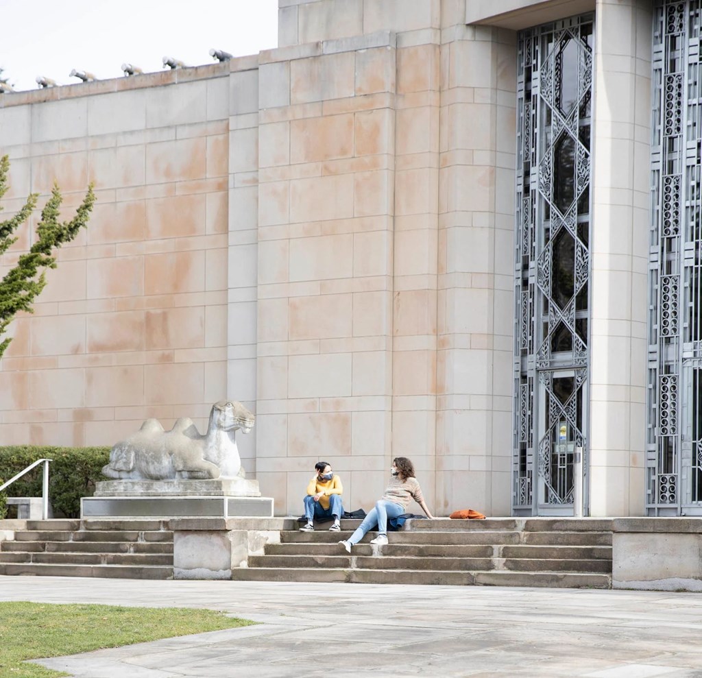Two people sitting on steps in front of a building with a lion statue.