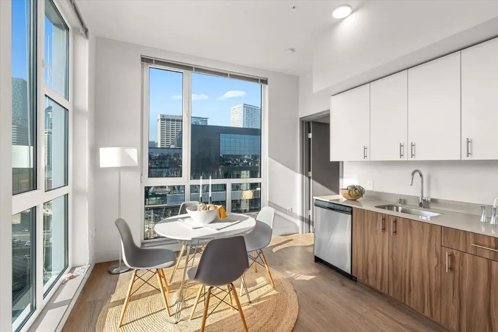 A modern kitchen with a dining table and chairs in front of a large window overlooking the city.
