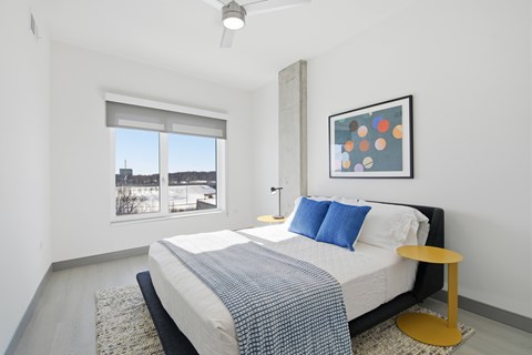 A bedroom with a bed, a window, and a painting on the wall.