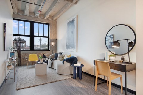 A living room with a yellow chair and a desk with a lamp.