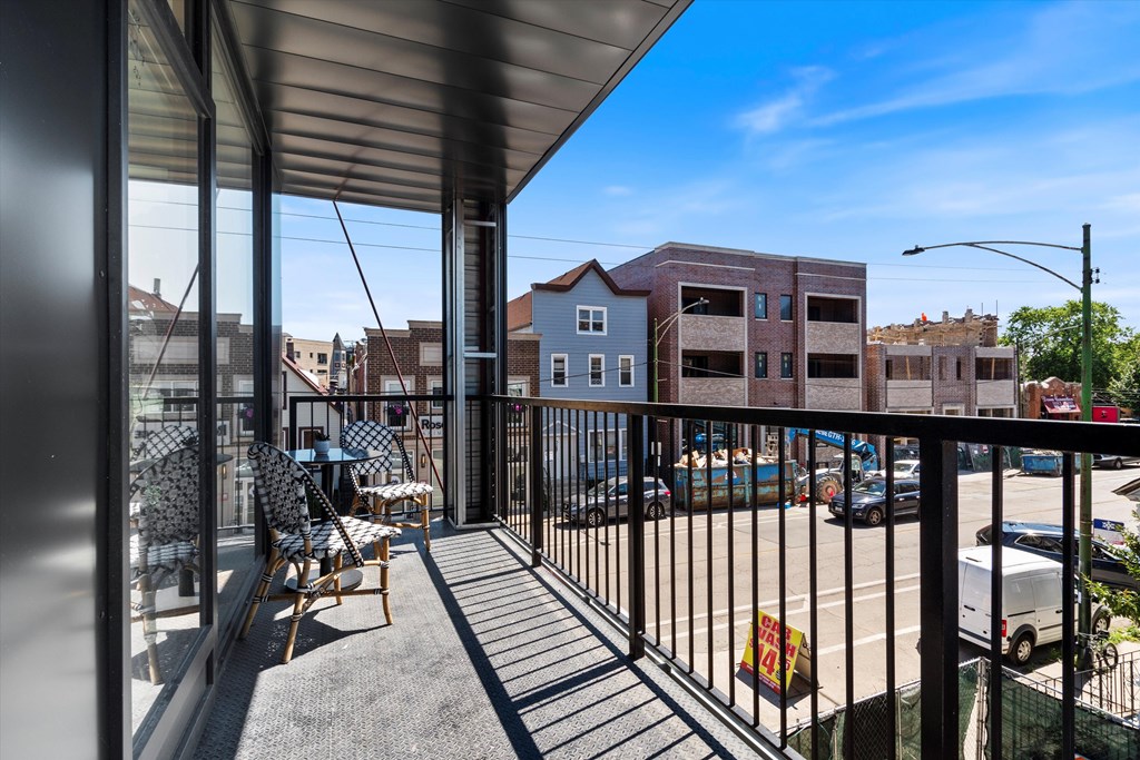 A balcony with a table and chairs overlooks a parking lot.