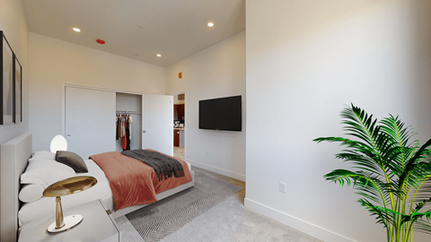 A bedroom with a bed, a chair, a plant, and a TV mounted on the wall.