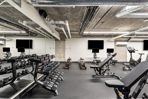 A gym with a variety of equipment including dumbbells, benches, and exercise bikes.