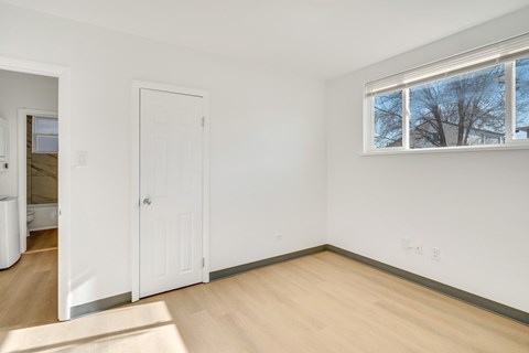 A room with a white door and a window with a view of trees outside.