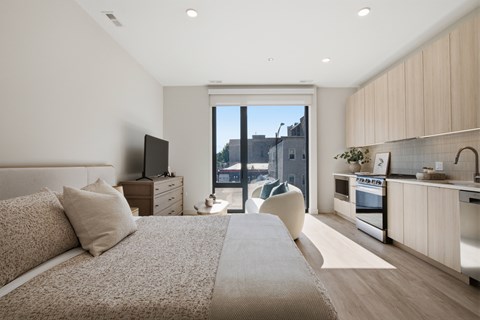 A modern bedroom with a large bed and a kitchen area in the background.