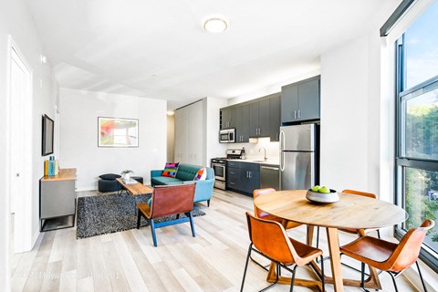 a living room with a table and chairs and a kitchen with stainless steel appliances