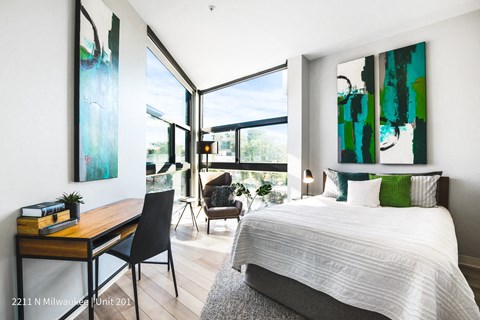 a bedroom with a bed and a desk and large windows