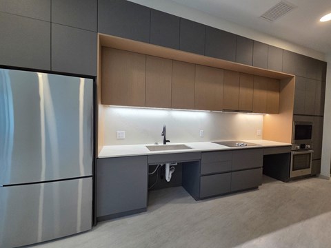 A modern kitchen with a refrigerator on the left and a counter with a sink in the middle.