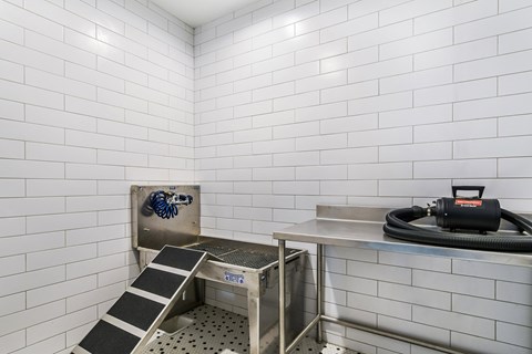 A white tiled room with a metal platform and a black hose.