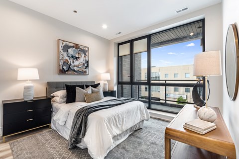 A bedroom with a large bed, a painting on the wall, and a view of the city.