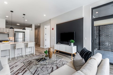 A modern living room with a white sofa, a glass coffee table, and a TV on a white cabinet.