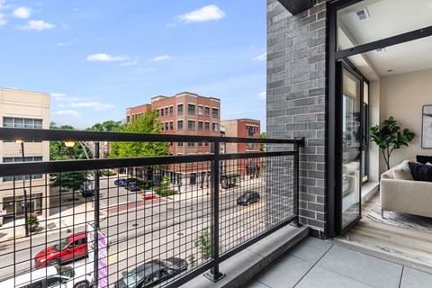 A balcony with a black railing overlooks a parking lot and buildings.