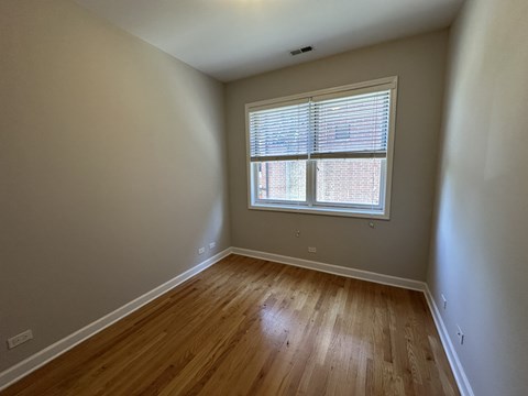 A room with wooden flooring and a window with blinds.