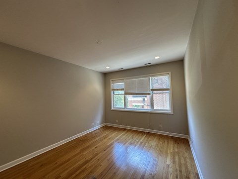 A room with wooden flooring and a window with blinds.