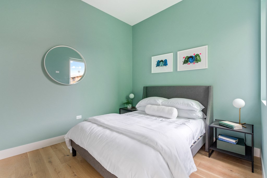 A bedroom with a bed, nightstand, lamp, and two pictures on the wall.