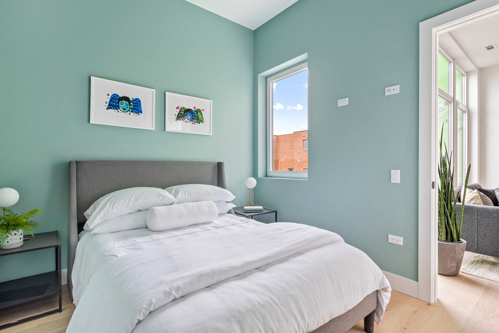 A bedroom with a bed, nightstand, and two pictures on the wall.