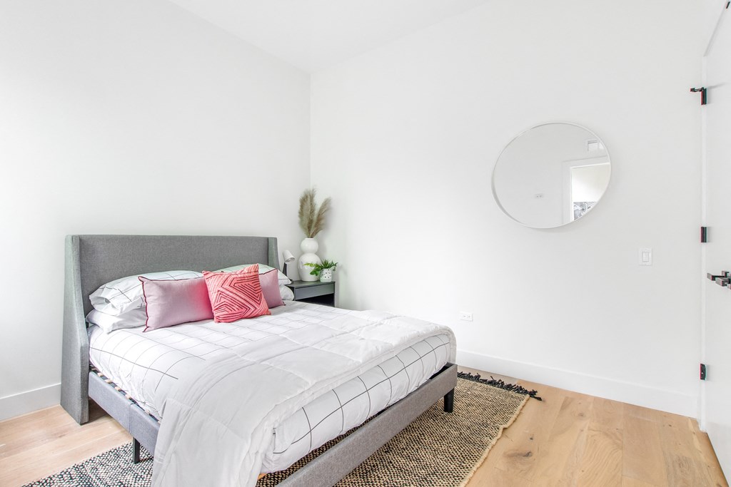 A bedroom with a bed, pillows, a mirror, and a rug.