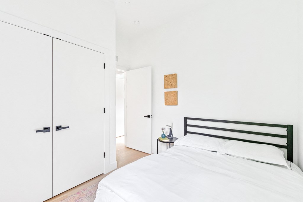 A white bedroom with a bed, nightstand, and two white doors.