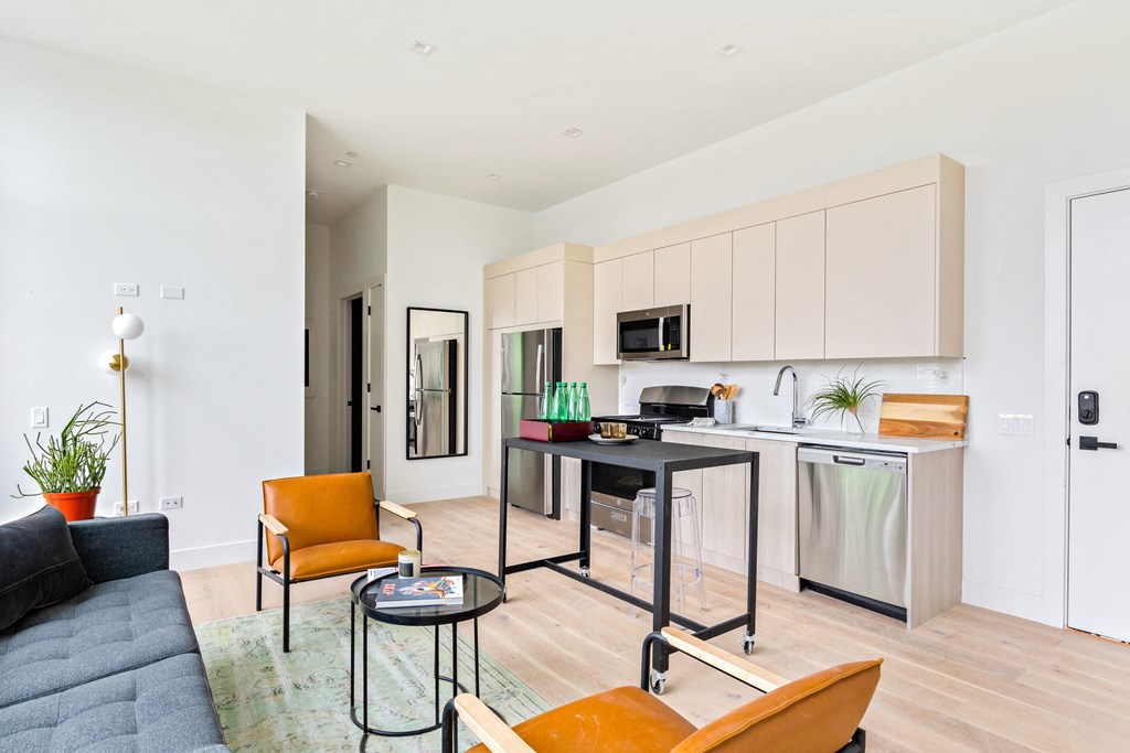 A modern kitchen with a black sofa and orange chairs.