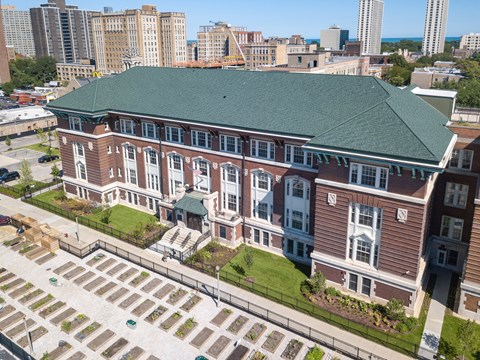 A large red brick building with a green roof and a parking lot in front.