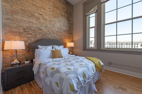 A bedroom with a brick wall and a large bed with a white and yellow comforter.