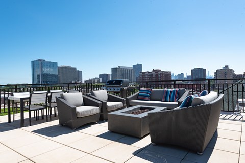 A patio with grey couches and a table with a fire pit in front of a city skyline.