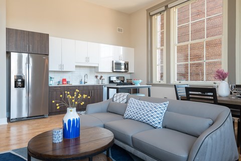 A modern kitchen with a grey couch and a wooden table.