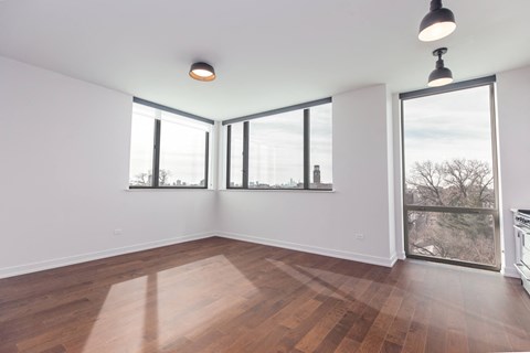 A room with wooden floors and white walls, with a large window and a view of trees outside.
