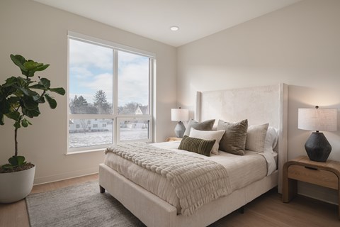 A bedroom with a large bed, a potted plant, and a view of a snowy landscape through the window.