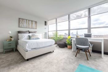 a bedroom with a bed and a desk in a room with large windows
