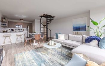 a living room with a couch and a kitchen with a spiral staircase