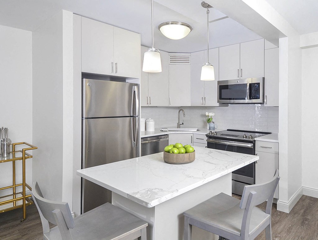 A modern kitchen with a white marble table and grey chairs.