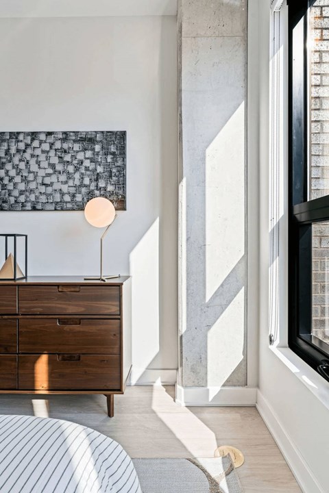 A modern bedroom with a wooden dresser and a large abstract painting on the wall.